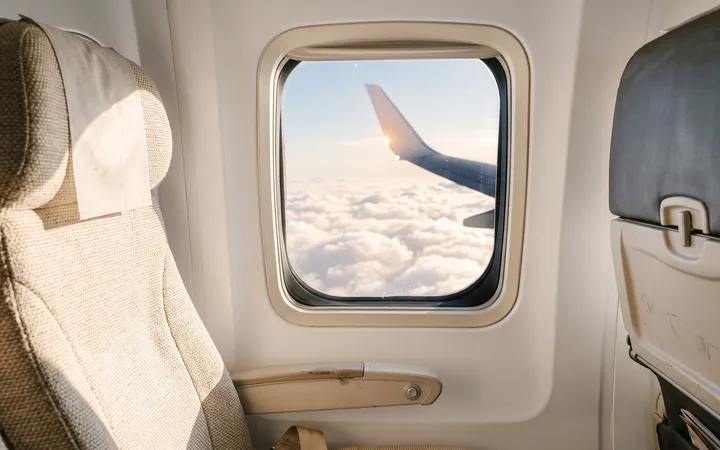 An airplane window seat in warm light with soft clouds outside.