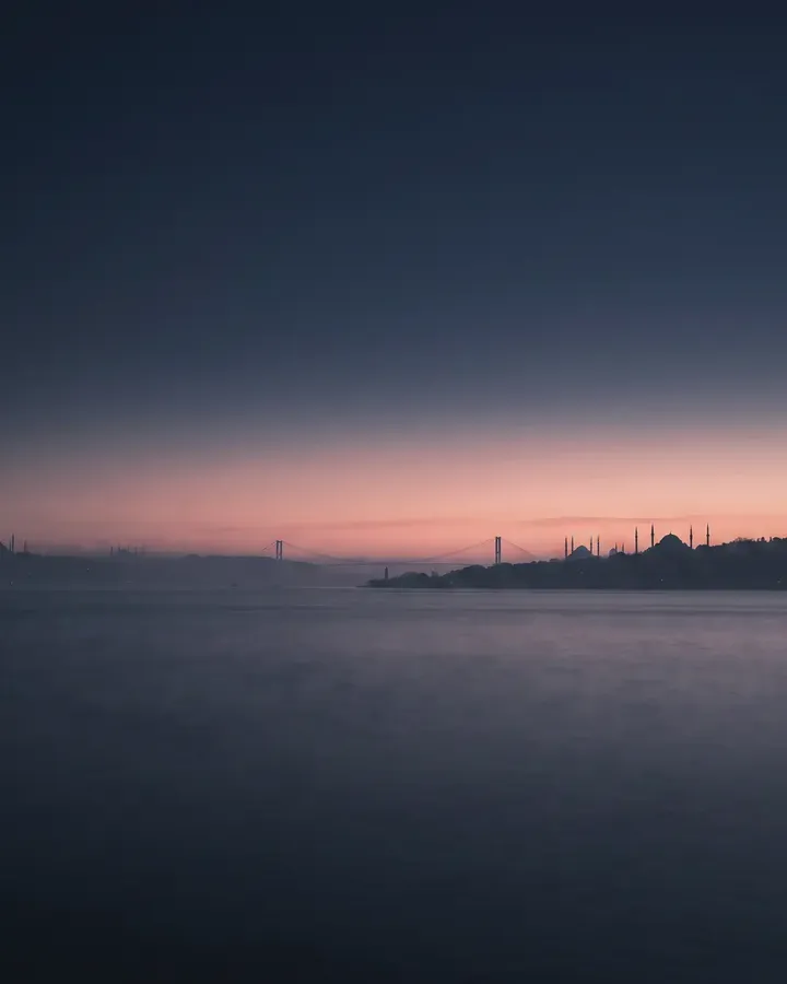 Alacakaranlıkta Boğaz'ın karşı kıyısından görünen İstanbul; köprü ve tarihi yarımada siluet hâlinde.